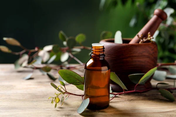Bottle of eucalyptus essential oil and plant branches on wooden table