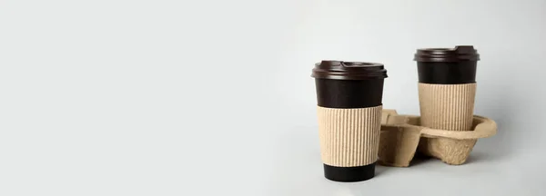 Takeaway paper coffee cups with sleeves, plastic lids and cardboard holder on light grey background, space for text. Banner design