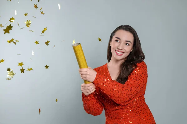 Young woman blowing up party popper on light grey background