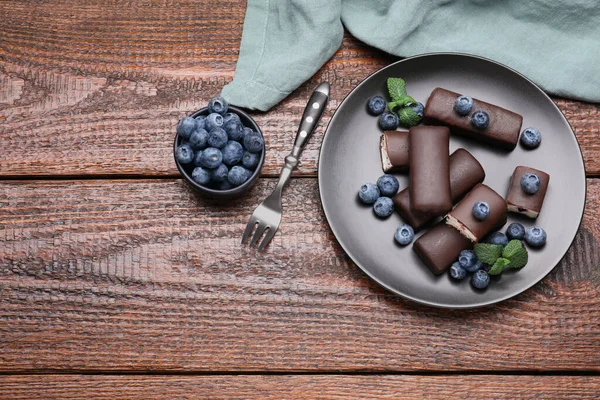 Delicious glazed curd snacks with blueberries on wooden table, flat lay. Space for text