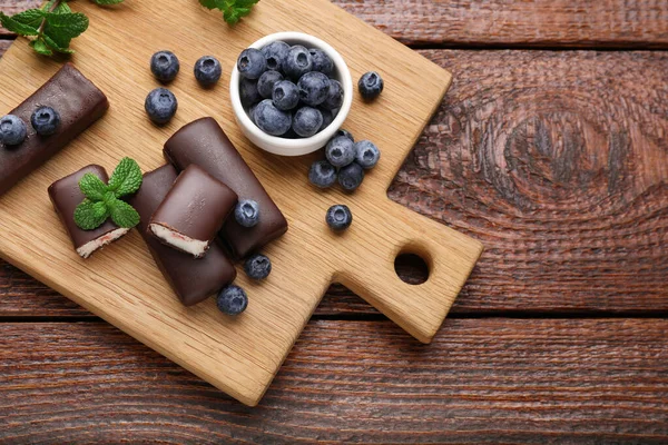 Delicious glazed curd snacks with fresh blueberries and mint on wooden table, top view. Space for text