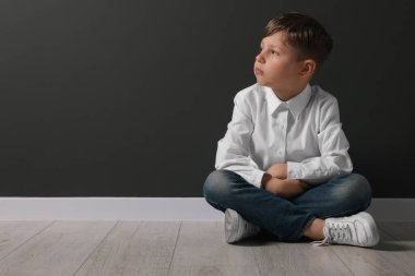 Küçük çocuk siyah duvarın yanında oturuyor, mesaj için yer var. Okul zorbalığı