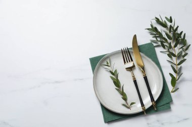 Çatal bıçak takımları ve okaliptüs yapraklarıyla beyaz mermer masa, düz. Metin için boşluk