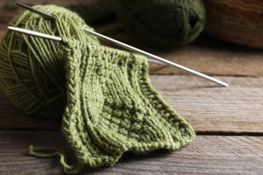 Yumuşak yeşil yün iplik, örgü ve iğneler ahşap masada, yakın plan