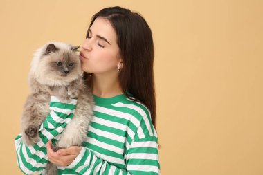 Açık kahverengi arka planda sevimli kedisini öpen bir kadın, mesaj için boşluk