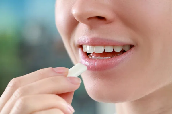 Woman putting chewing gum piece into mouth on blurred background, closeup