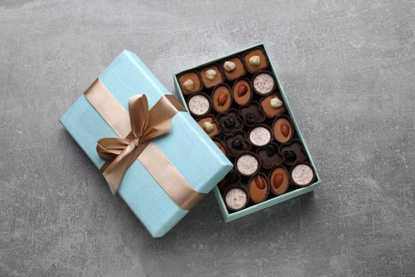 Open box of delicious chocolate candies on light grey table, top view