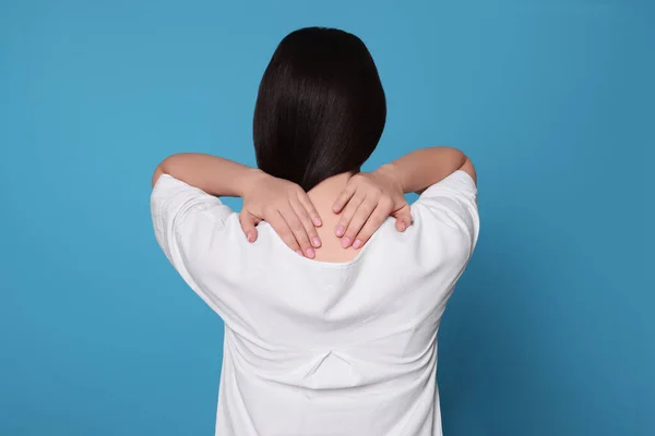 ライトブルーの背景に首の痛みに苦しんでいる若い女性 バックビュー 関節炎の症状 — ストック写真