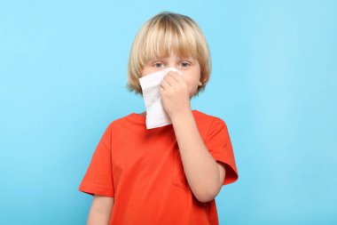 Açık mavi arka planda burnu dokuya sümküren çocuk. Soğuk belirtileri