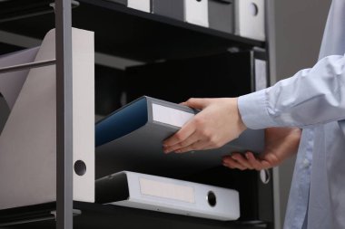 Woman taking folder with documents from shelf in office, closeup