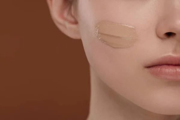 Teenage girl with swatch of foundation on face against brown background, closeup
