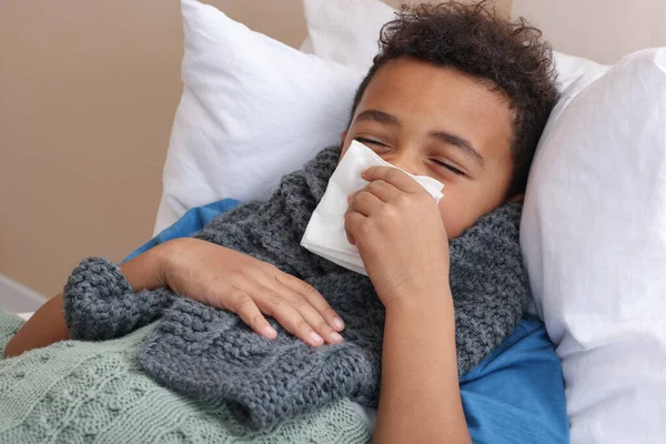 アフリカ系アメリカ人の少年で スカーフと組織がベッドの中で鼻を吹いている 風邪の症状 — ストック写真