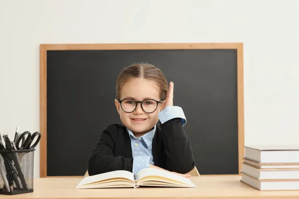 Šťastný Malý Školní Dítě Zvedá Ruku Zatímco Sedí Stolem Knihami — Stock fotografie