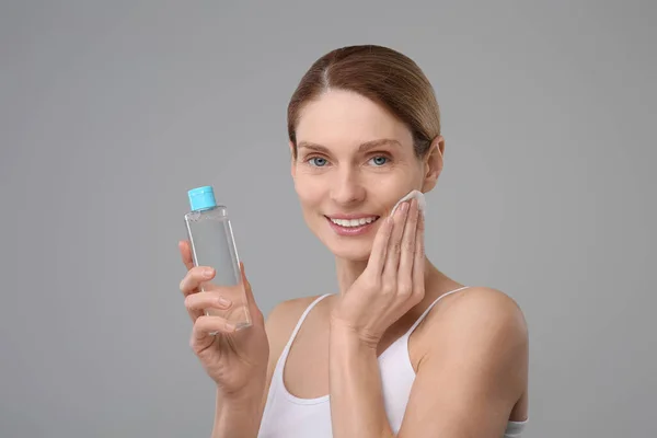 stock image Beautiful woman removing makeup with cotton pad on gray background