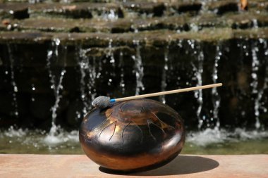 Steel tongue drum with mallet near waterfall outdoors on sunny day. Percussion musical instrument clipart