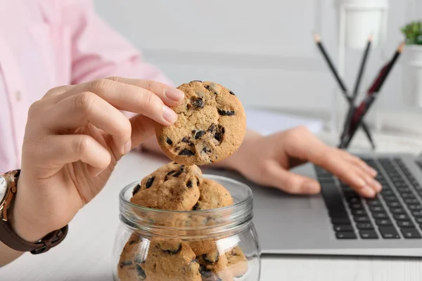 Office worker taking chocolate chip cookie from jar at workplace, closeup