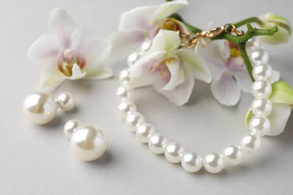 Κομψά Σκουλαρίκια Μαργαριτάρι Βραχιόλι Και Ορχιδέα Λουλούδια Λευκό Φόντο Closeup — Φωτογραφία Αρχείου