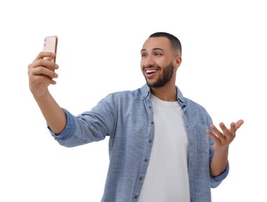 Gülümseyen genç adam beyaz arka planda akıllı telefonuyla selfie çekiyor.