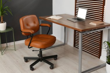 Rahat koltuk, masa ve dizüstü bilgisayarı olan şık bir ofis.