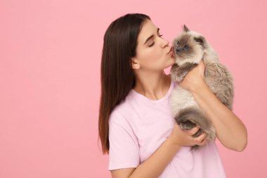 Güzel kedisini pembe arka planda öpen bir kadın, mesaj için boşluk.