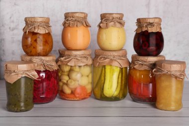 Birçok cam kavanoz ve ahşap masada farklı korunmuş ürünler.