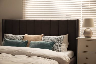 Odadaki beyaz çekmecelerin üzerinde yastıklar ve lambalar olan rahat bir yatak. Şık iç mekan