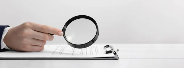 stock image Woman looking at documents through magnifier at white table, closeup. Banner design with space for text