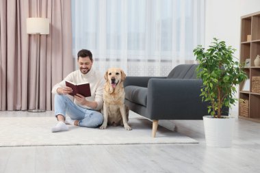 Adam yerde kitap okuyor. Evindeki şirin Labrador Retriever 'ının yanında.
