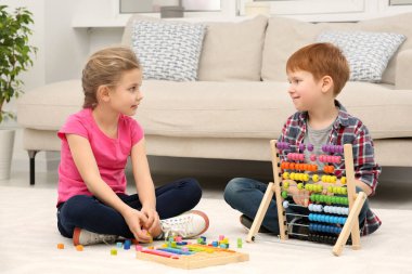 Çocuklar oturma odasında yerde farklı matematik oyun setleriyle oynuyorlar. Matematiği zevkle çalış
