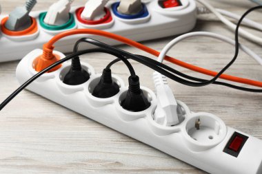 Beyaz ahşap zeminde uzantı kabloları olan güç şeridi, yakın plan. Elektrikçi ekipmanı.