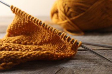 Yumuşak turuncu örgü ve ahşap masa üzerinde metal iğneler, yakın plan.
