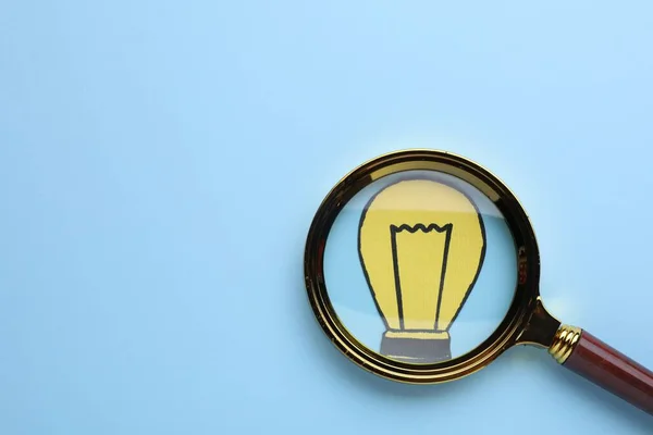Magnifying glass over paper light bulb on blue background, top view. Space for text