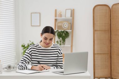 Çevrimiçi çeviri kursu. Evde dizüstü bilgisayarın yanında yazan öğrenci