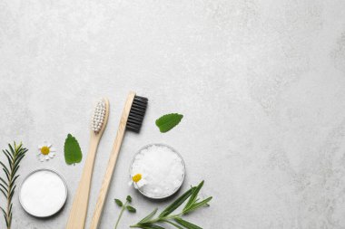 Bambu diş fırçaları, çiçekler ve bitkiler açık gri masada, düz yerde. Metin için boşluk