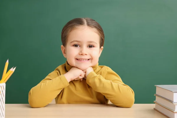 stock image Happy little school child sitting at desk with books near chalkboard