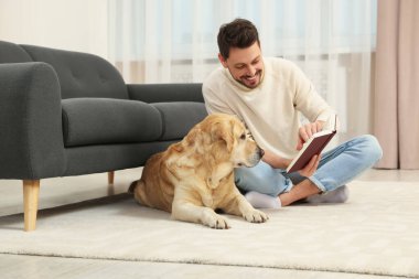 Adam yerde kitap okuyor. Evindeki şirin Labrador Retriever 'ının yanında.