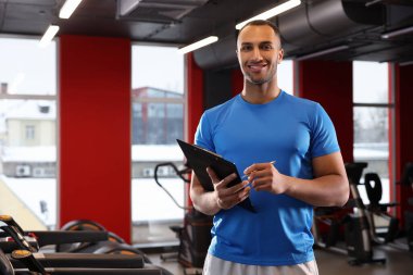 Happy trainer writing down workout plan in modern gym, space for text