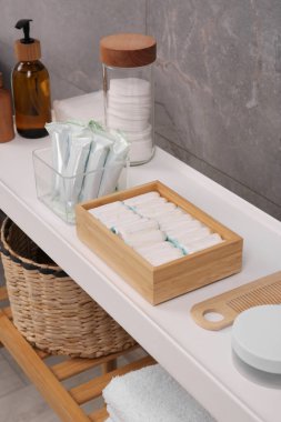 Gri duvarın yanındaki beyaz masada birçok farklı tampon ve kişisel bakım ürünleri var.