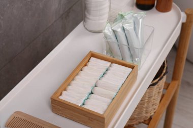 Gri duvarın yanındaki beyaz masada birçok farklı tampon ve kişisel bakım ürünleri var.