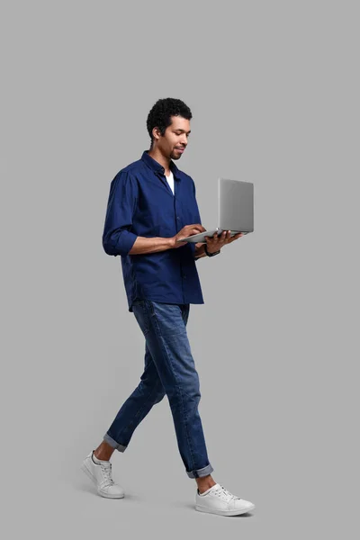 灰色の背景を歩きながらノートパソコンを使うハンサムな男 — ストック写真
