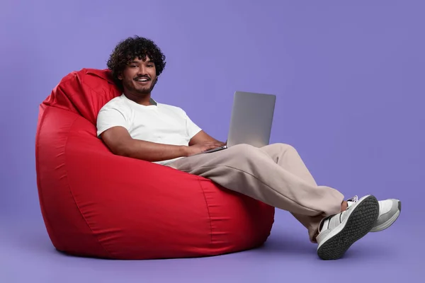 Lachende Man Met Laptop Zittend Zitzak Stoel Tegen Paarse Achtergrond — Stockfoto
