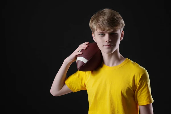 stock image Teenage boy with american football ball on black background. Space for text