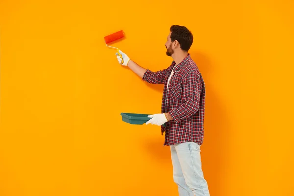 设计师在橙色墙壁上涂上染料滚筒 案文的篇幅 — 图库照片
