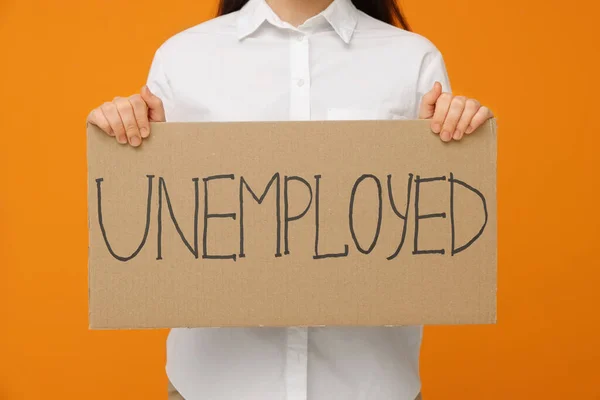 オレンジの背景に失業者という言葉で看板を持っている若い女性 クローズアップ — ストック写真
