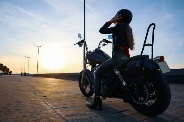 Woman in helmet sitting on motorcycle at sunset. Space for text