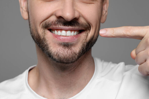 Man showing healthy gums on gray background, closeup