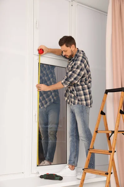 Man measuring window with tape indoors. Roller blinds installation