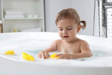 Evinde köpüklü banyoda lastik ördekleri olan sevimli küçük kız.