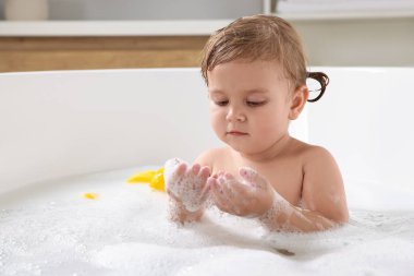 Şirin küçük kız evde köpüklü banyo yapıyor.