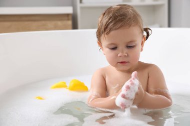 Şirin küçük kız evde köpüklü banyo yapıyor.